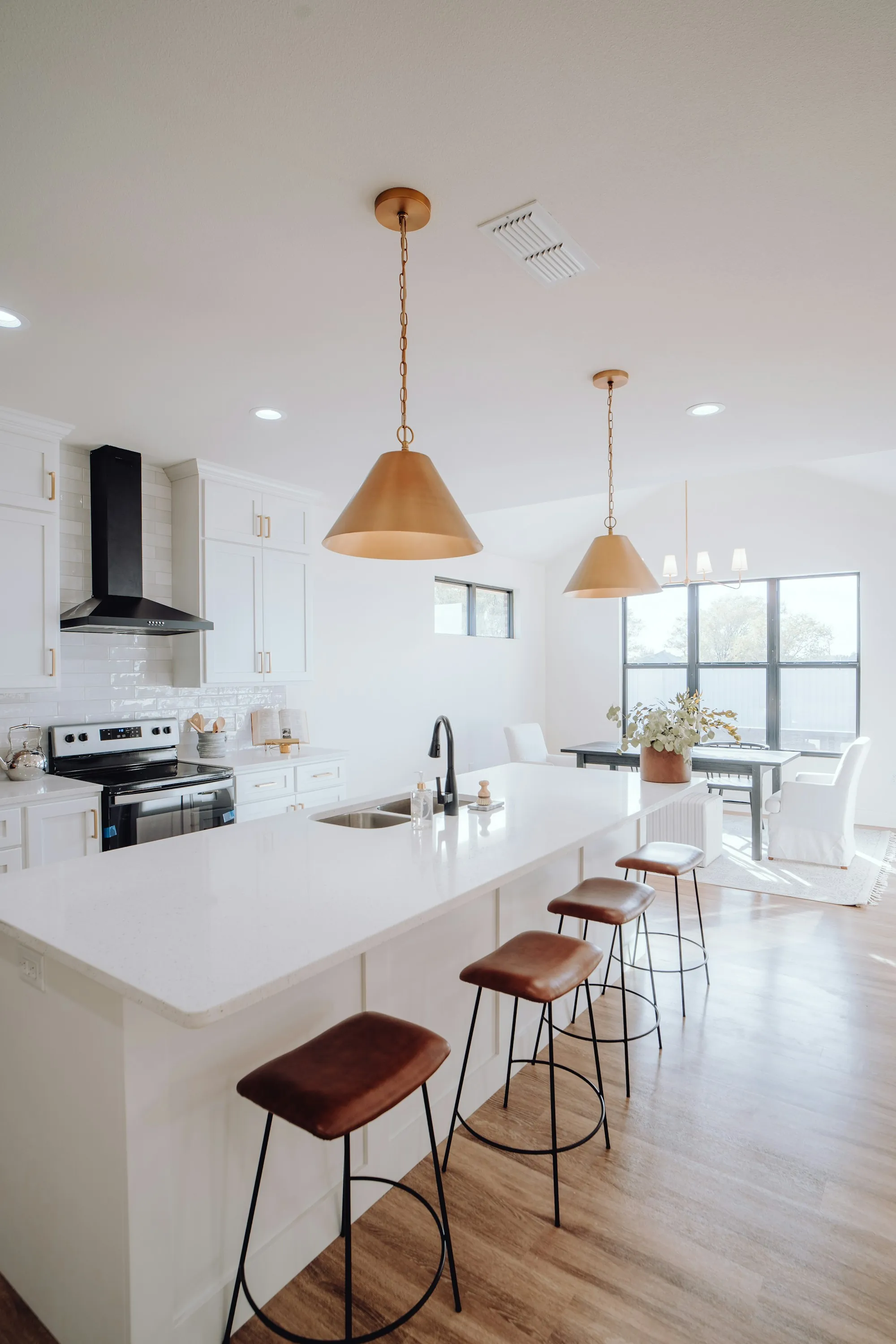 Bright white kitchen with a long island, brass pendant lights and bar stools